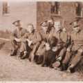 Soldiers sit on a wall outside what looks like a barracks