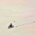 A guy on a bike razzes down the face of a huge dune