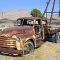 An old 50s Chevrolet pickup rusts away near a railroad and farmyard