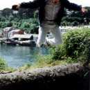 John leaps off a wall, just on the other side of the river from Fowey