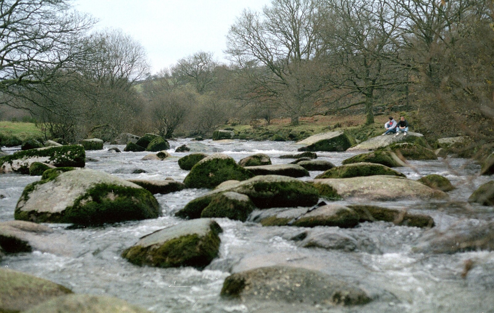 Riki and Andy sit on the rocks and watch the river from Uni: A Trip to Venford Resevoir, Dartmoor, Devon - 18th January 1987