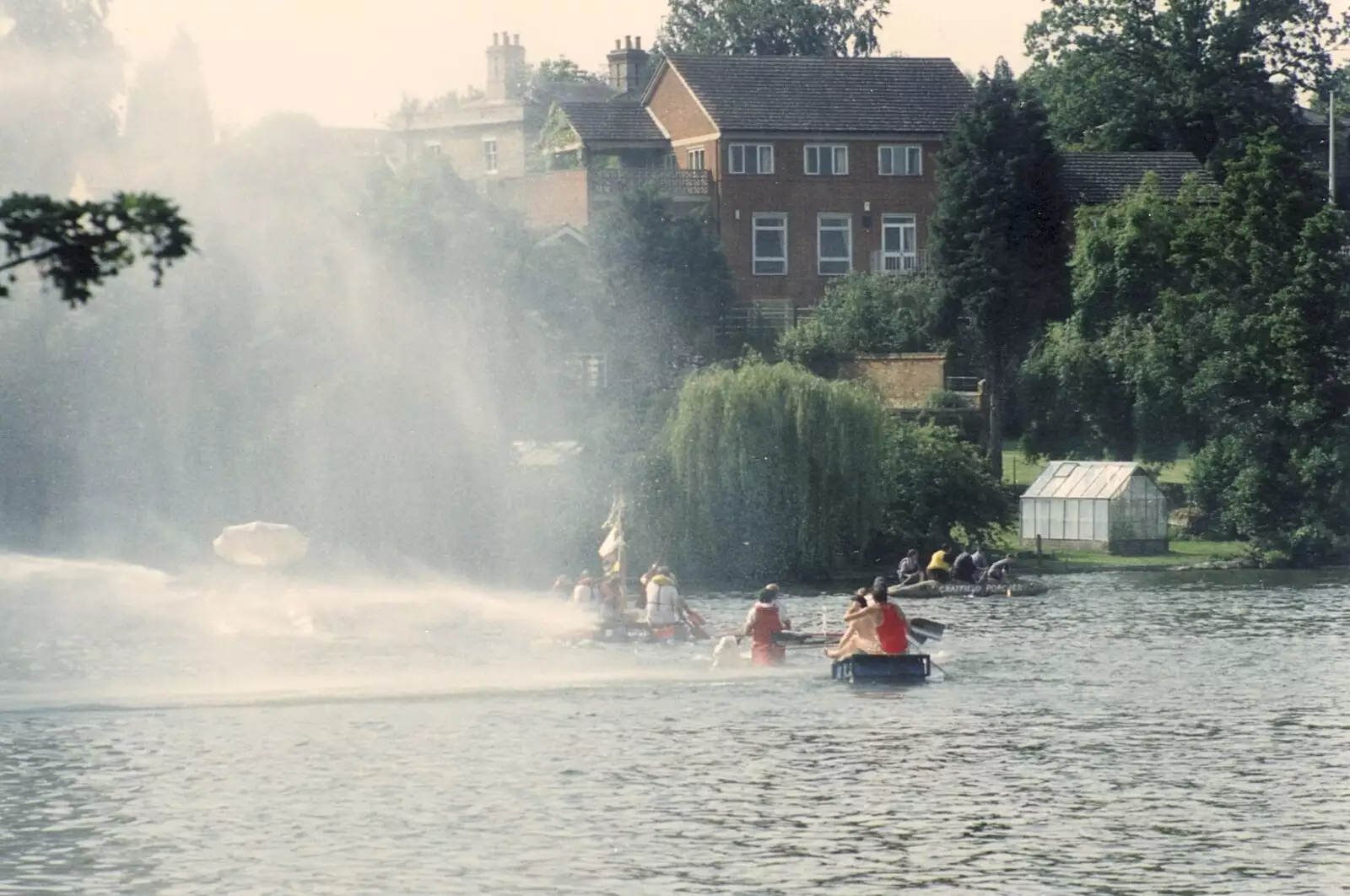 The rafts paddle through a wall of spray from firehoses, from A Raft Race on the Mere, Diss, Norfolk - 2nd June 1990