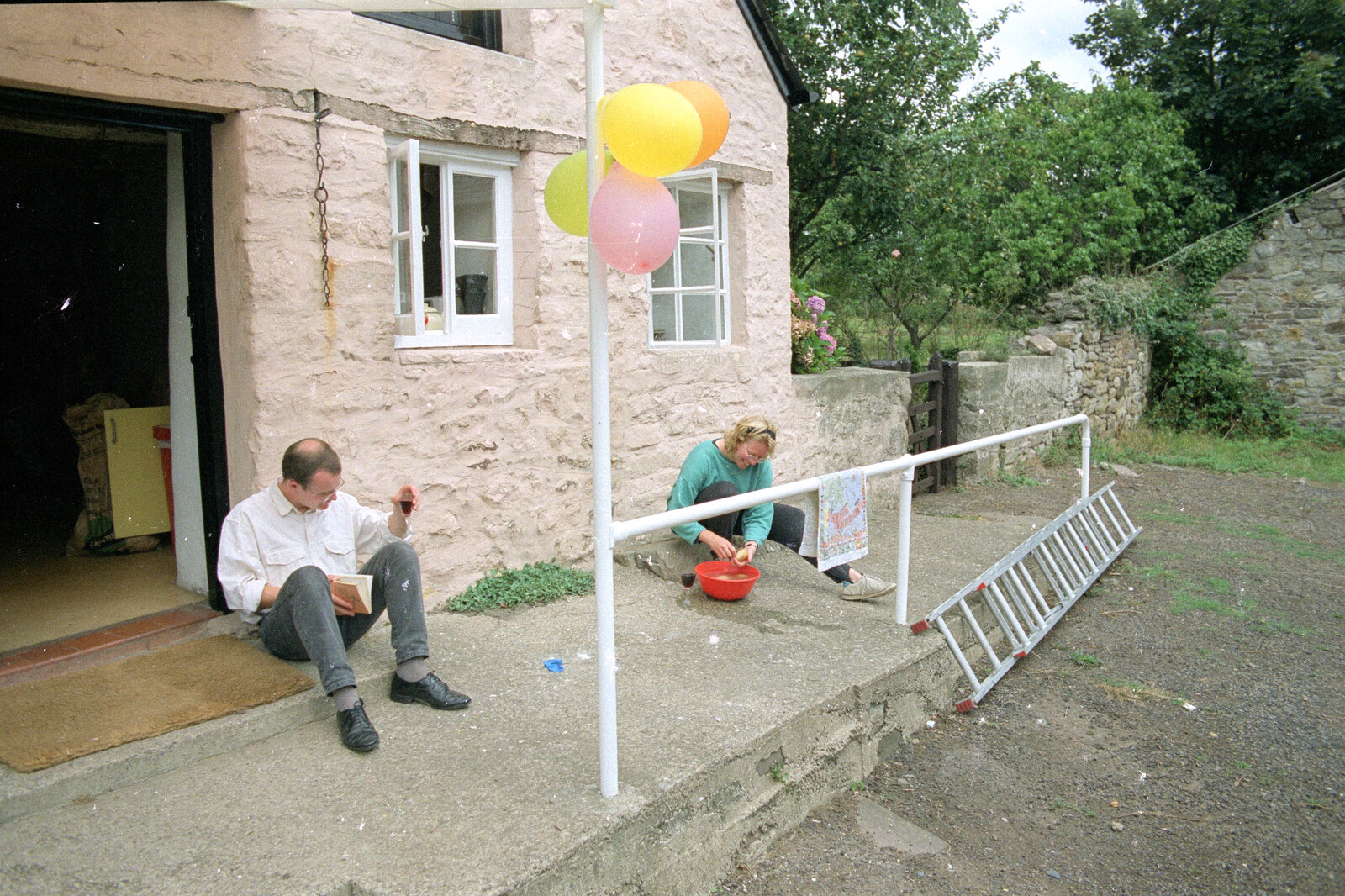 Liz's Party, Abergavenny, Monmouthshire, Wales - 4th August 1990: Hamish reads whilst Liz peels potatoes