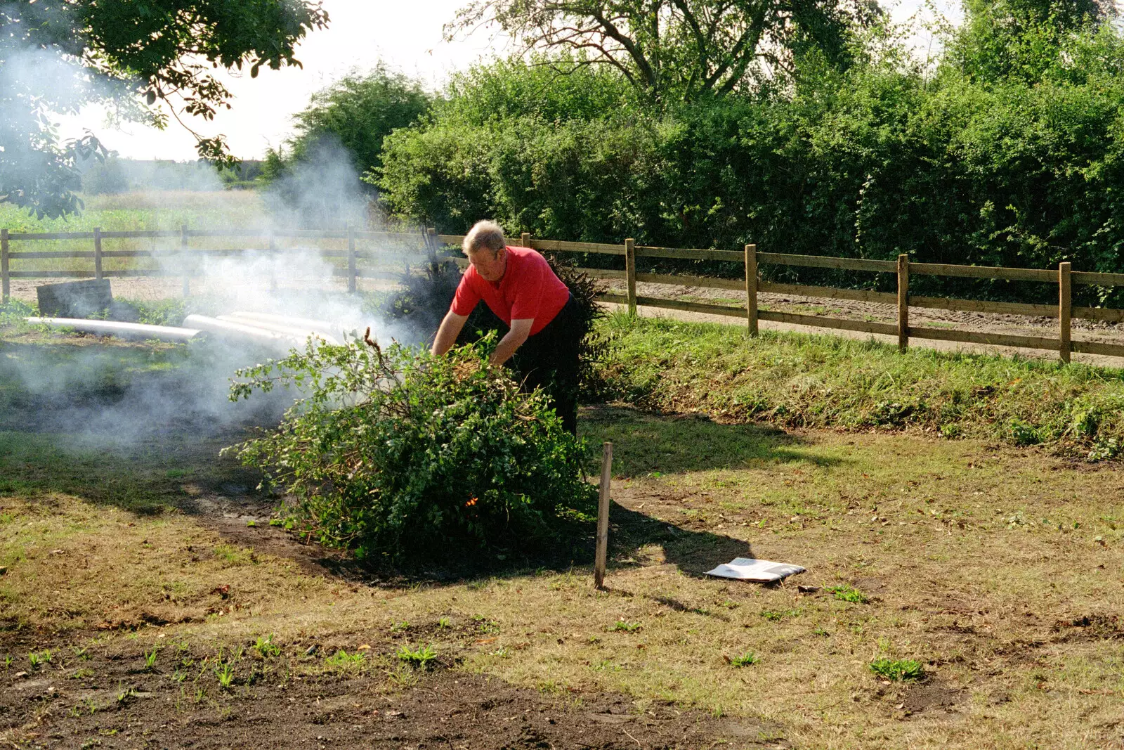 Tony hurls a bush onto the bonfire, from Tony and Janet's Building Plot, and the Red Arrows, Eye, Suffolk - 22nd July 1998