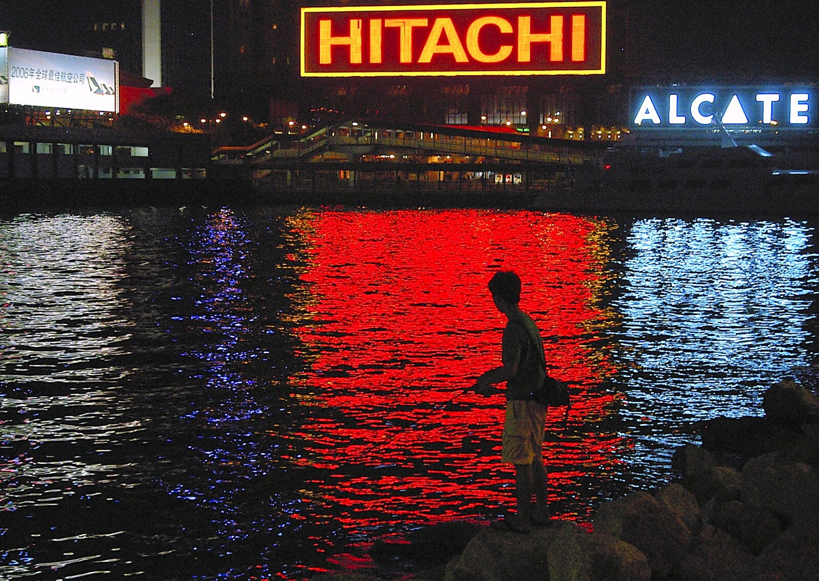 A boy fishes in the harbour, backlit by neon from Wan Chai and Central, Hong Kong, China - 2nd October 2006