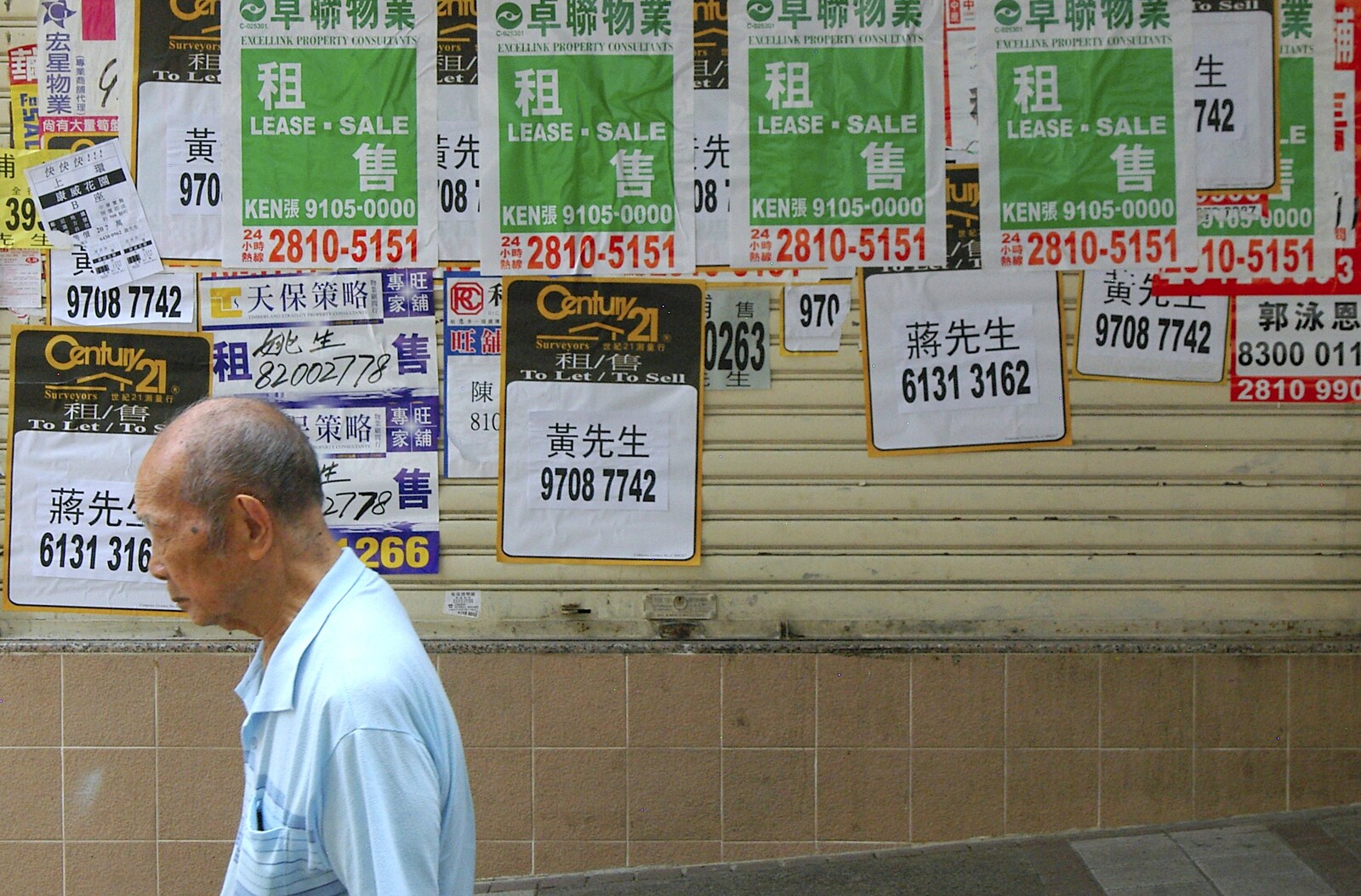 An old dude walks past posters from Wan Chai and Central, Hong Kong, China - 2nd October 2006