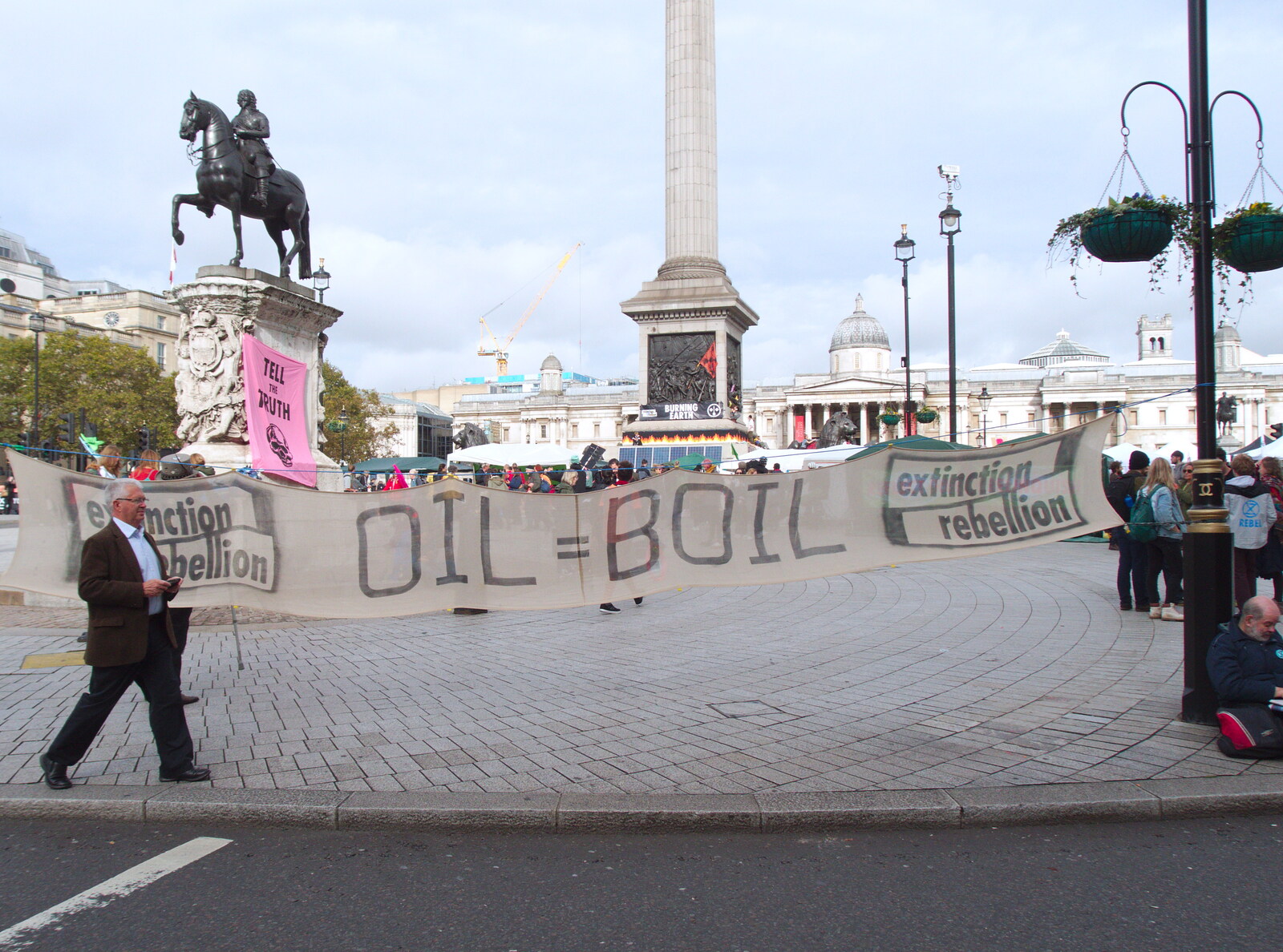 A businessman walks past an oil=boil banner from The Extinction Rebellion Protest, Westminster, London - 9th October 2019